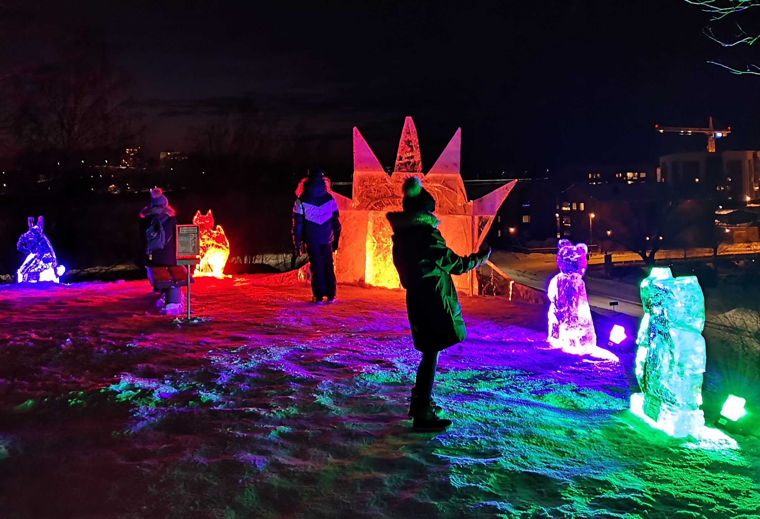 Värivaloin valaistuja jääveistoksia Lappeenrannan linnoituksessa sekä ihmisiä ihailemassa teoksia.
